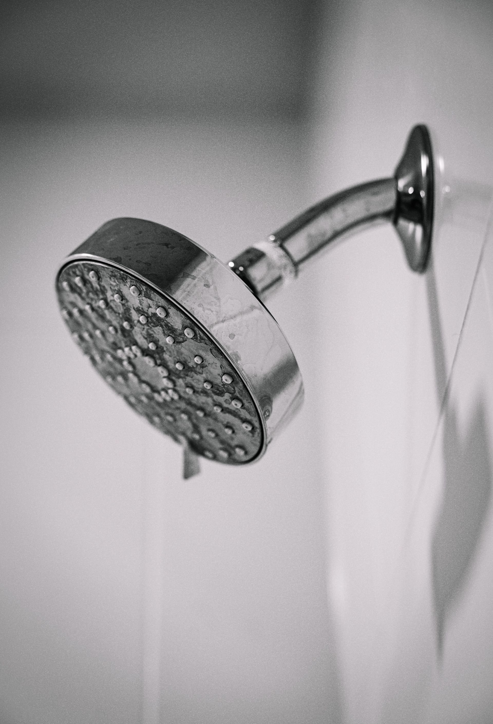 Black and white photo of a sleek, metal showerhead mounted on a bathroom wall.